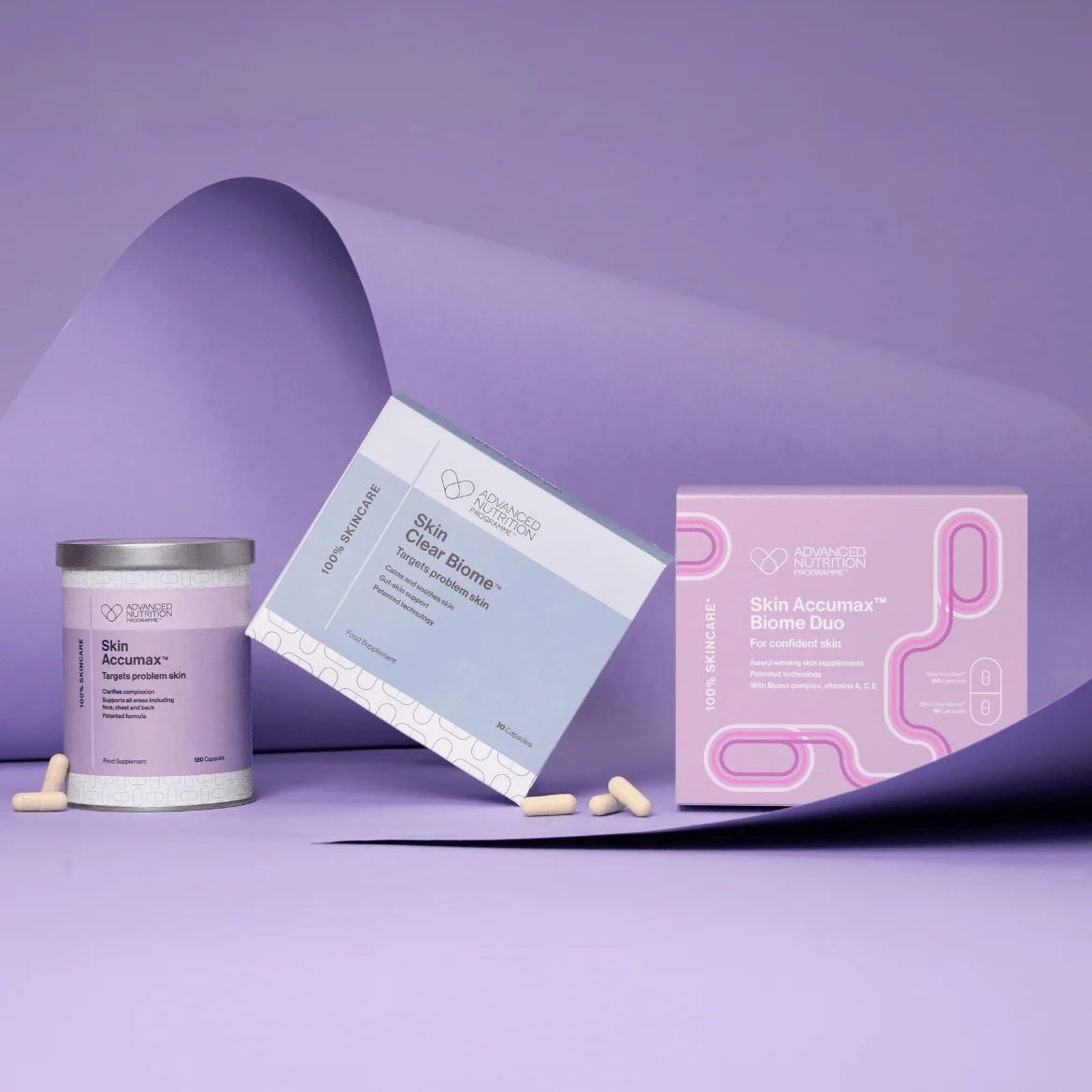 A skincare product set on a lavender studio background, featuring a white jar labeled Skin Reset, a light blue box labeled Skin Barrier, and a pink box labeled Skin Acne Mask, with a few beige capsules scattered in front.